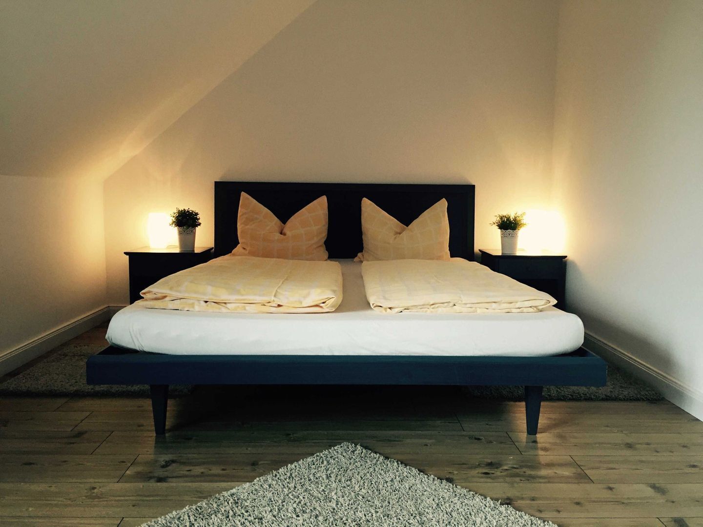 A bed with a dark headboard, two bedside tables with lamps, and a white rug on the floor.