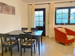 Ein Essbereich mit Tisch und Stühlen, ein rotes Sessel und ein Fenster mit Vorhängen.