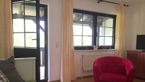 A room with a green sofa, a red armchair, a wooden table, and a window with curtains.