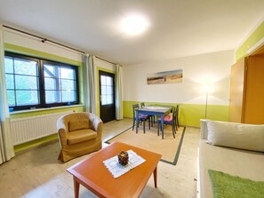 Quarto com poltrona marrom, mesa de madeira com objeto decorativo, mesa de jantar com cadeiras e sofá verde.