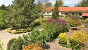 A landscaped garden with various trees and shrubs, a paved driveway, and a building with a red-tiled roof.
