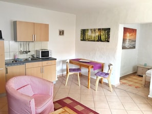 Un espacio habitable compacto con kitchenette, un comedor con dos sillas, un sofá y una pequeña mesa.