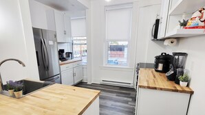 A modern kitchen with a central island, white cabinetry, and a view of the street through a large window.