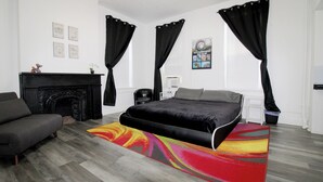 A modern bedroom with a large bed, a fireplace, a sofa, and a colorful rug.