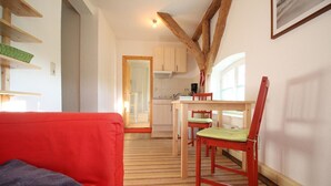 Een gezellige zithoek met een rode bank, houten vloeren en een eettafel met stoelen.