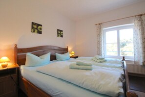 A neatly made bed with pillows and folded towels, a wooden headboard, bedside lamps, and two framed pictures on the wall. - Gutshof Dubnitz -Holiday apartment 5 Dörthe Dubnitz near Sassnitz - Gutshof Dubnitz (Sassnitz)