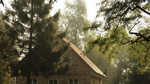 Een stenen huis met een puntgevel, omgeven door bomen en een gazon.