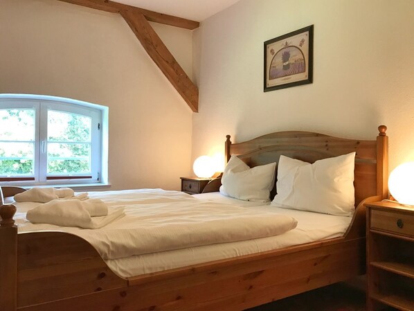 Un dormitorio con una cama de madera, ropa de cama blanca, un ventanal con vistas y un cuadro en la pared.