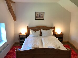 Cama doble con cabecera de madera, dos mesitas de noche con lámparas, un cuadro enmarcado en la pared y una ventana con vistas.