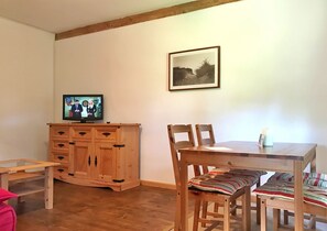Un comedor con una mesa y sillas de madera, un televisor sobre un mueble de madera, y un cuadro enmarcado en la pared.