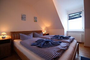 A bedroom with a sloped ceiling, two beds with checkered bedding, bedside lamps, and a window with sheer curtains.