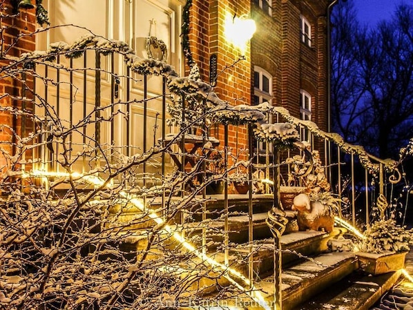 A snow-covered outdoor staircase with a railing, surrounded by bare trees and a brick building in the background.