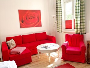 Una stanza con un divano rosso, una poltrona rossa, un tavolino da caffè bianco e un quadro di una rosa appeso al muro.