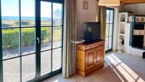 Amplia habitación con grandes puertas corredizas de vidrio que dan a un jardín, un mueble de madera con un televisor y una chimenea decorada con adornos.