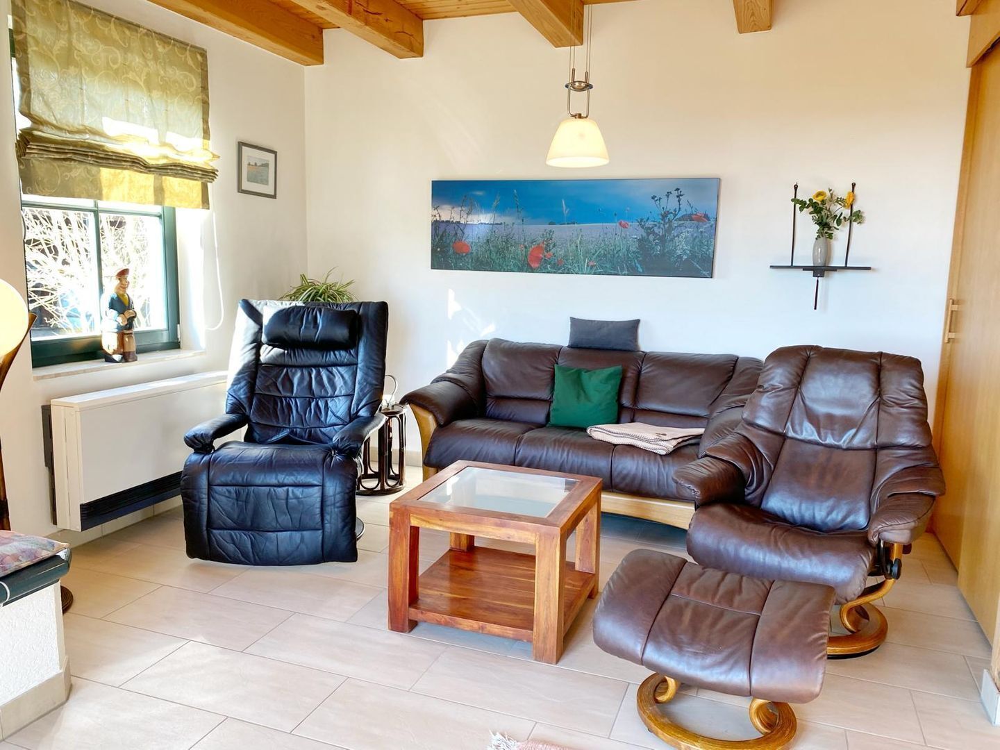 A living room with a leather sofa, a recliner, and a coffee table. There is a painting on the wall and a window with a view of trees.