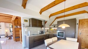 Una cocina moderna con armarios oscuros, encimera blanca y horno empotrado. Cuenta con un comedor con mesa y sillas blancas.