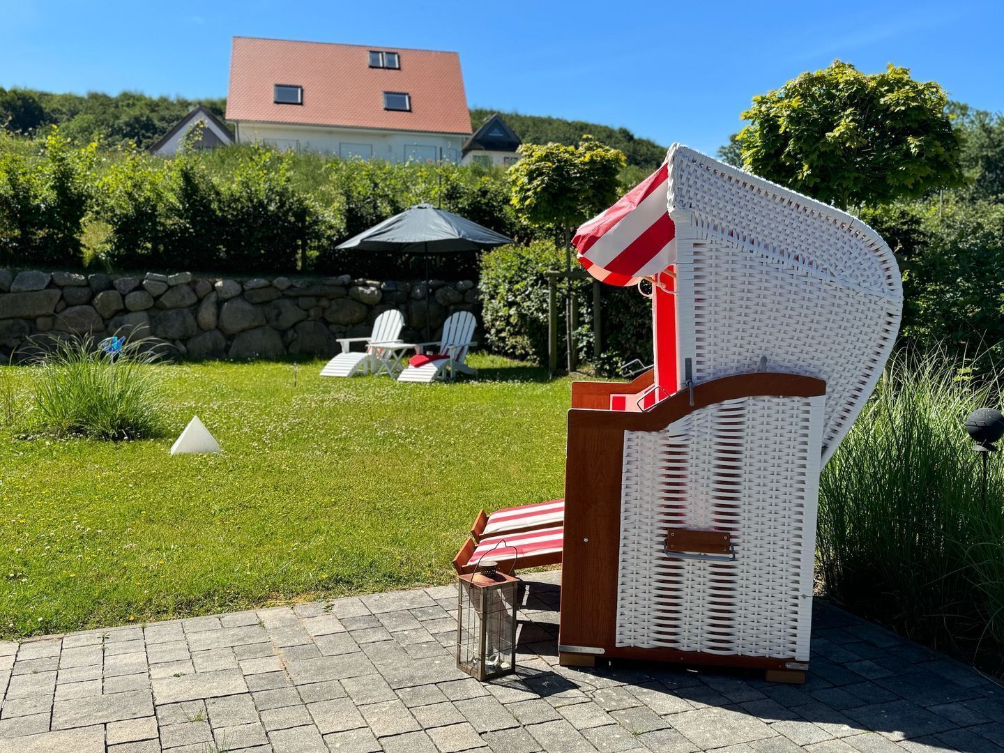 Une chaise en osier, un parasol à rayures rouges et blanches, un mur de pierre et une maison en arrière-plan.