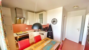 A compact kitchen with white cabinets, a wooden table, red chairs, and a clock on the wall.