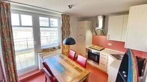 A compact kitchen with a dining table, red chairs, a stove, and a window with curtains.
