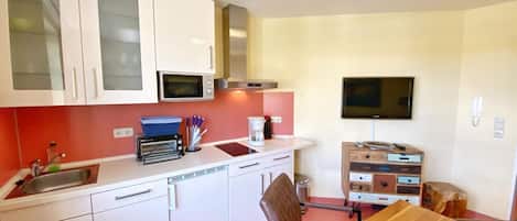 Een kleine keuken met witte kastjes, een magnetron, een broodrooster en een koffiezetapparaat.