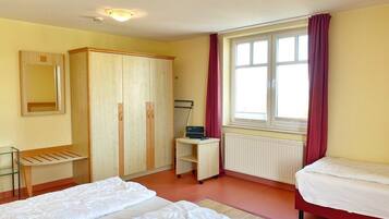 Ein Schlafzimmer mit zwei Betten, einem Schrank, einem Schreibtisch, einem Stuhl, einem Heizkörper und einem Fenster mit Vorhängen.