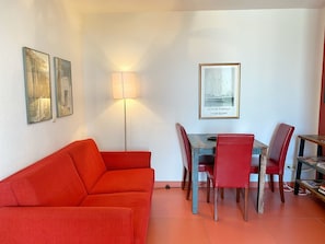 Un comedor con una mesa y sillas, un sofá rojo y cuadros en la pared.