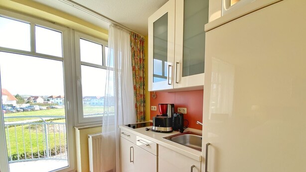 A kitchen with white cabinets, a window with a view of houses, and a radiator.