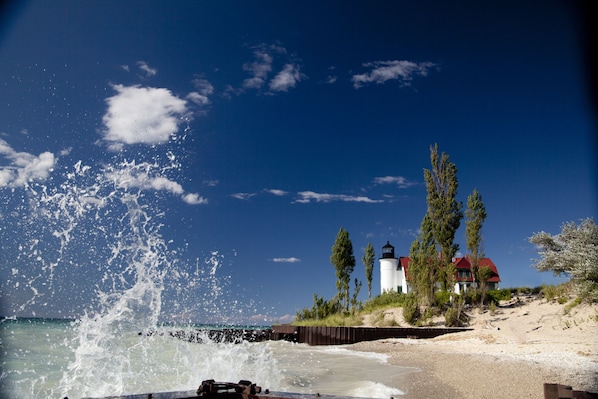 Une plage où les vagues se brisent sur le rivage, un phare et une maison avec un toit rouge.