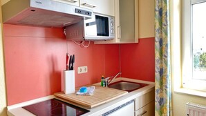 A compact kitchen with a red backsplash, a microwave, a built-in stove, and a small sink. - Apartment 307 - Rondell an der Jasmundtherme - Neddesitz an der Jasmundperle / (Sagard)