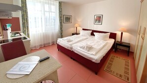 A hotel room with a bed, two bedside tables with lamps, a desk with a chair, a window with sheer curtains, and a small rug on the floor. - Apartment 307 - Rondell an der Jasmundtherme - Neddesitz an der Jasmundperle / (Sagard)