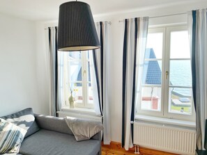 A room with a grey sofa, a hanging lamp, and a view of the sea through large windows. - Seaside Appartements, "Grey" - Sassnitz - Seaside Appartements (Sassnitz)