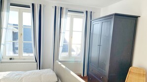Ein Schlafzimmer mit zwei Betten, einem Kleiderschrank, einem Sessel und großen Fenstern mit Vorhängen.