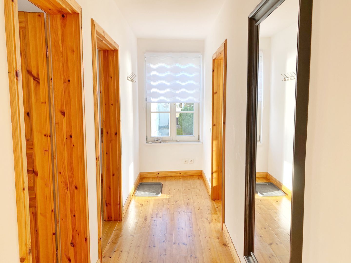 A narrow hallway with wooden doors and a window with wavy blinds.
