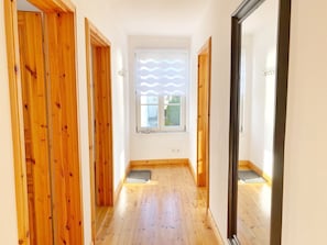 Un couloir étroit avec des portes en bois et une fenêtre ornée de stores à lamelles ondulées.