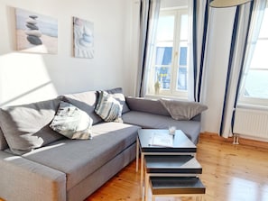 Un salon moderne avec un canapé gris, des coussins à rayures, une petite table en bois et une fenêtre avec des rideaux.