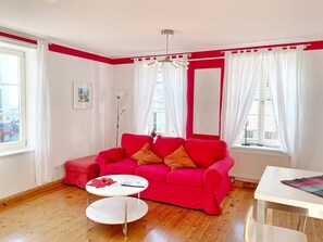 A bright living room with a red sofa, a white coffee table, and a white dining table. - Seaside Appartements, "Red" - Sassnitz - Seaside Appartements (Sassnitz)