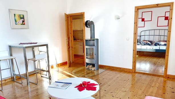 Een moderne woonkamer met een ronde witte tafel, een rode bank en een keuken die zichtbaar is door een open deur.