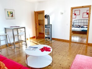 A modern living room with a round white table, a red couch, and a kitchen area visible through an open door. - Seaside Appartements, "Red" - Sassnitz - Seaside Appartements (Sassnitz)