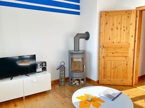 A room with a TV, a wood-burning stove, a wooden door, and a small table with a candle.