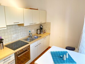 A modern kitchen with white cabinets, a stainless steel sink, a coffee maker, and a stove. - Seaside Appartements, "Dark Blue" - Sassnitz - Seaside Appartements (Sassnitz)