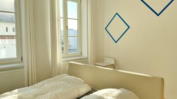 Ein Schlafzimmer mit zwei Einzelbetten, einem Heizkörper, einem Fenster mit Vorhängen und einem Sessel.