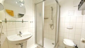 Une salle de bain moderne avec une douche à parois de verre, un lavabo blanc, des toilettes et un miroir dont le cadre est en bois.
