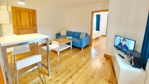 Un salon moderne avec un plancher en bois, un canapé bleu, une table basse blanche, un meuble TV blanc et un coin repas avec une table blanche et des chaises en métal.