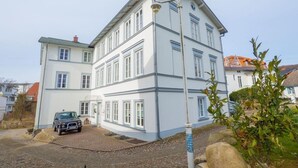 Un immeuble à plusieurs étages, doté d’une façade blanche et de bordures bleues, une allée pavée et une voiture garée.