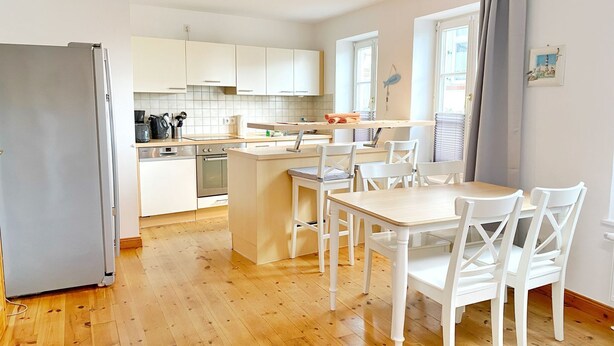 A modern kitchen with white cabinets, a central island, and a dining area with white chairs.