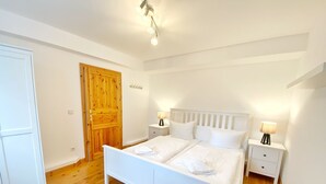 A bedroom with a white bed, two bedside tables, a wooden door, and a light fixture on the ceiling.