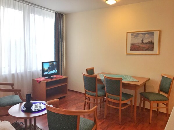 Una habitación acogedora con una mesa de madera, cuatro sillas, un televisor en un mueble bajo y un cuadro enmarcado en la pared.