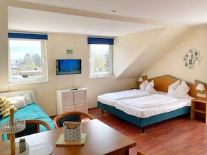 A bedroom with a bed, a desk, a chair, a television, and a window.
