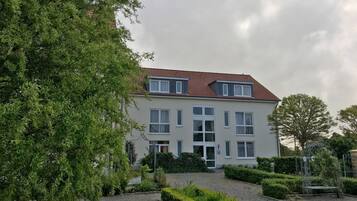 Un bâtiment à deux étages, doté d’un toit recouvert de tuiles rouges, de nombreuses fenêtres et d’un jardin bien entretenu avec des haies et un chemin de gravier.