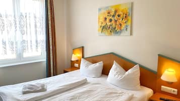 Ein Hotelzimmer mit einem aufgeräumten Bett, zwei Nachttischlampen, einem Sonnenblumenbild an der Wand und einem Fenster mit Vorhängen.